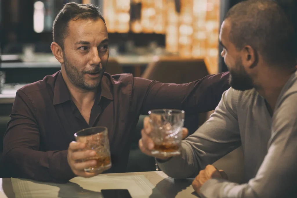 Zwei männliche Freunde verbringen Zeit miteinander in einer Bar oder Kneipe. Erwachsene Männer halten Gläser mit Whiskey oder Brandy. Freunde kommunizieren und sprechen mit Kristallgläsern in den Händen.